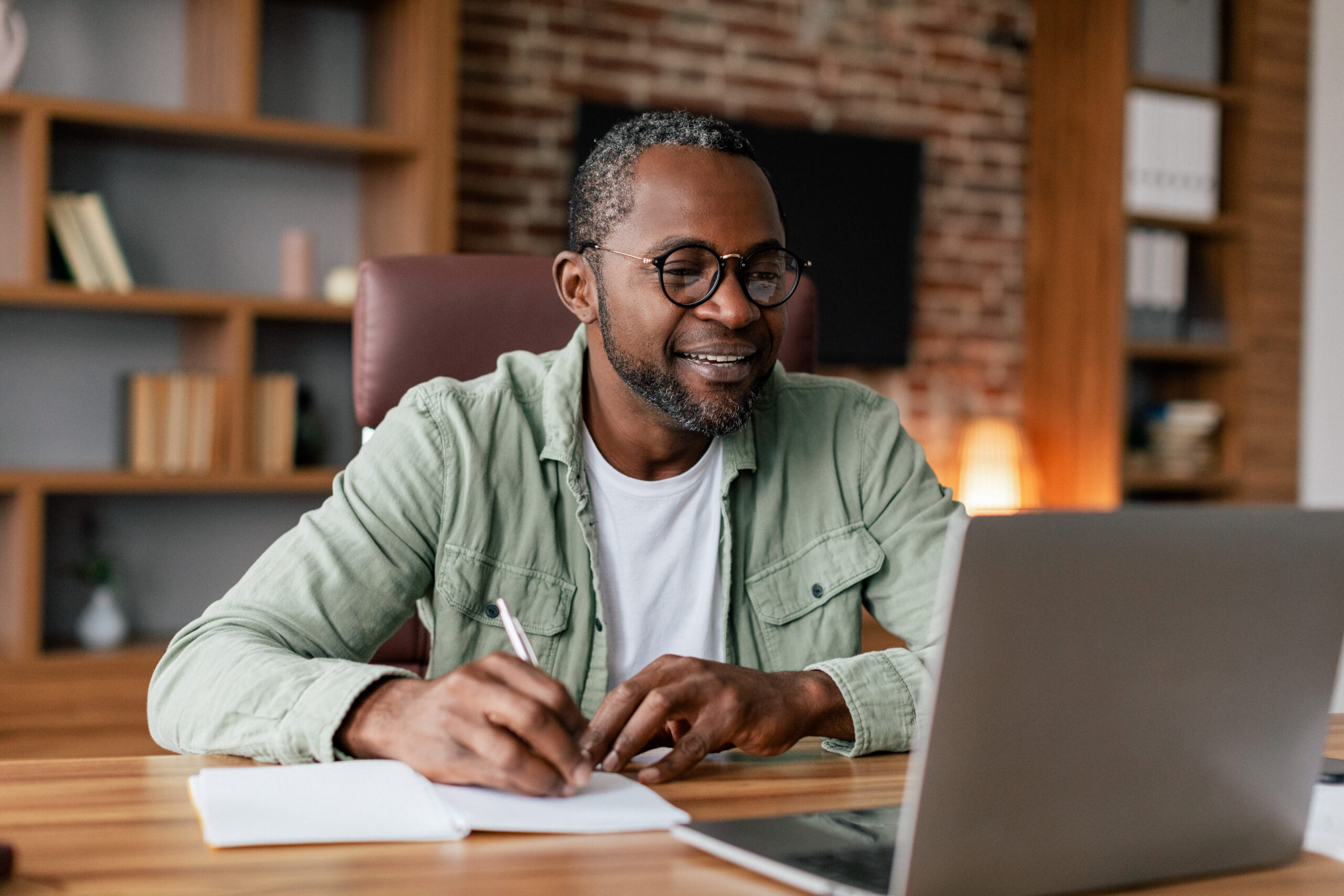 Smiling middle aged african american male in glasses and casual working on laptop in home office interior